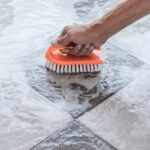 Man's hand cleaning ceramic tile with a brush and soapy water