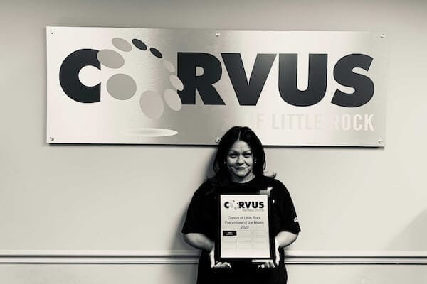 Corvus of Little Rock Franchisee Laura Torres - Black & White photo standing in front of Corvus sign