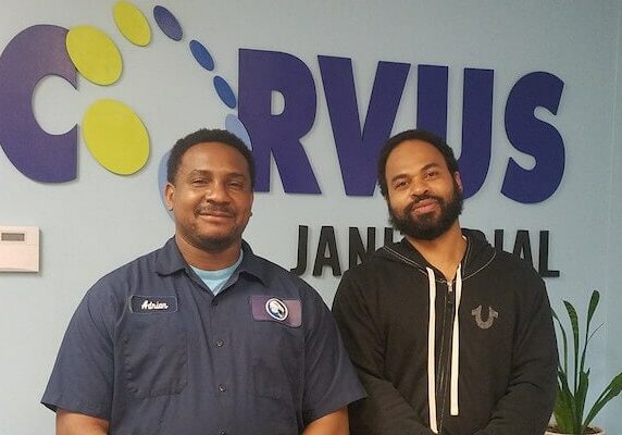 Two Corvus of St. Louis Franchise Owners (Darren Starks & Adrian West) pose for photo in front of Corvus sign