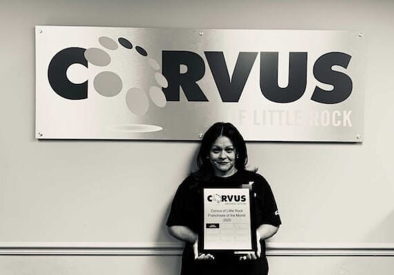 Corvus of Little Rock Franchisee Laura Torres - Black & White photo standing in front of Corvus sign