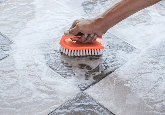 Man's hand cleaning ceramic tile with a brush and soapy water